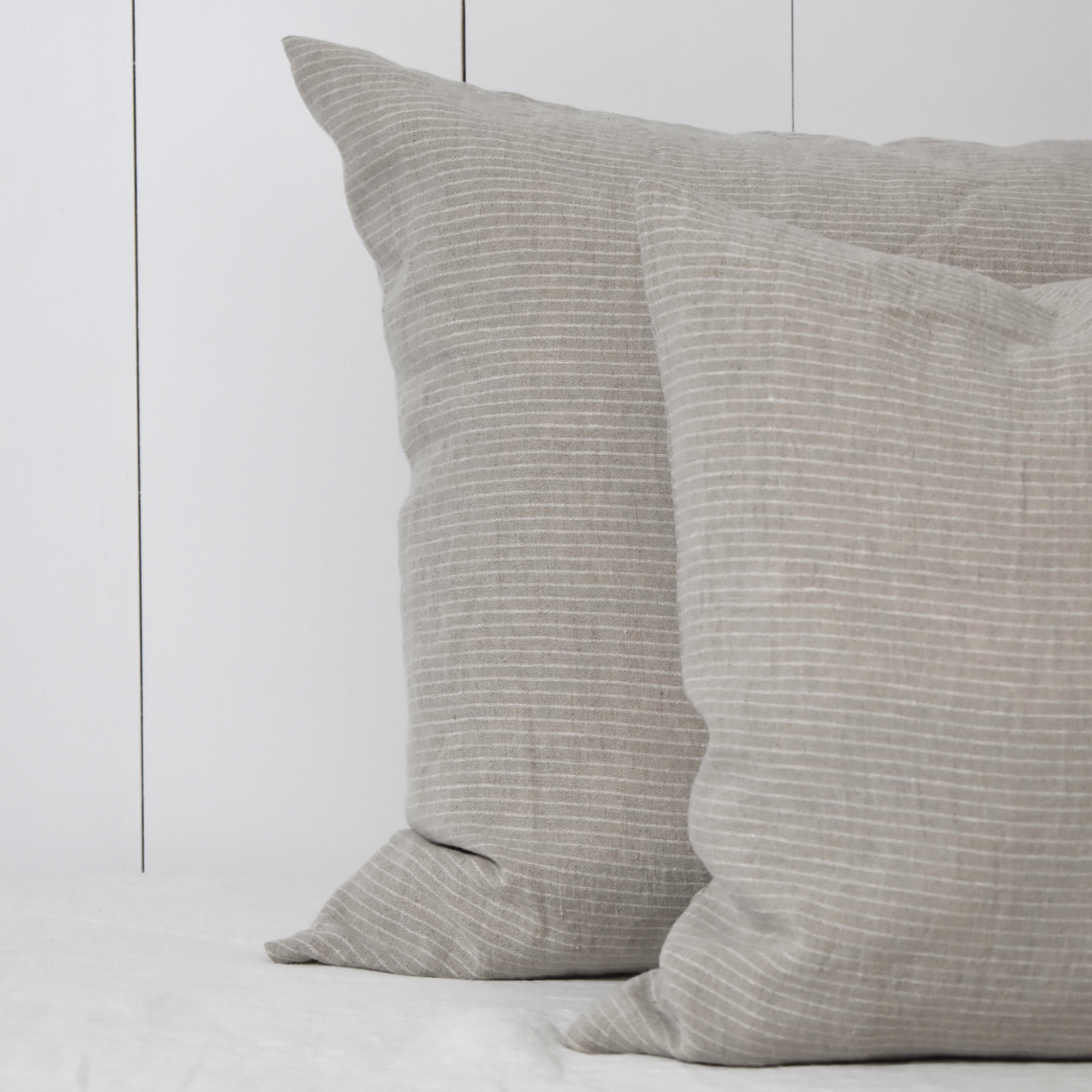 Twee vlaskleurige linnen kussenslopen met een subtiel off white streepje op bed.