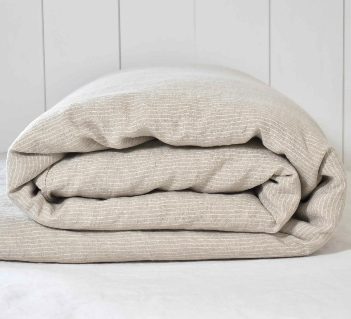 Duurzaam opgevouwen dekbedovertrek van gewassen linnen in de originele, ongeverfde vlaskleur naturel met een off-white streepje.