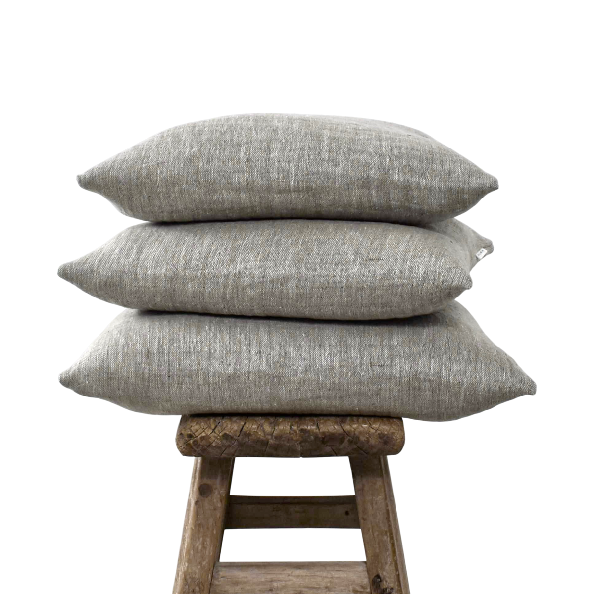 Stapel van drie linnen kussenslopen in de tweekleurige tint Coconut double woven op een verweerd houten krukje tegen een witte achtergrond.