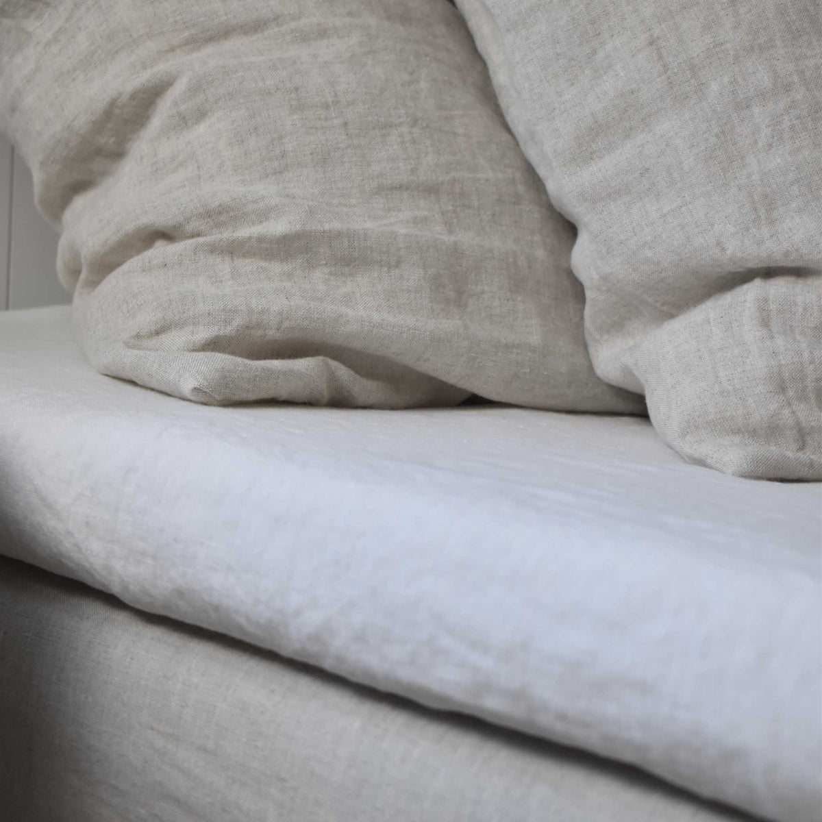 Close-up van gewassen linnen beddengoed met een wit hoeslaken en beige linnen kussensloop in Scandinavische stijl.