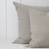 Twee vlaskleurige linnen kussenslopen met een subtiel off white streepje op bed.